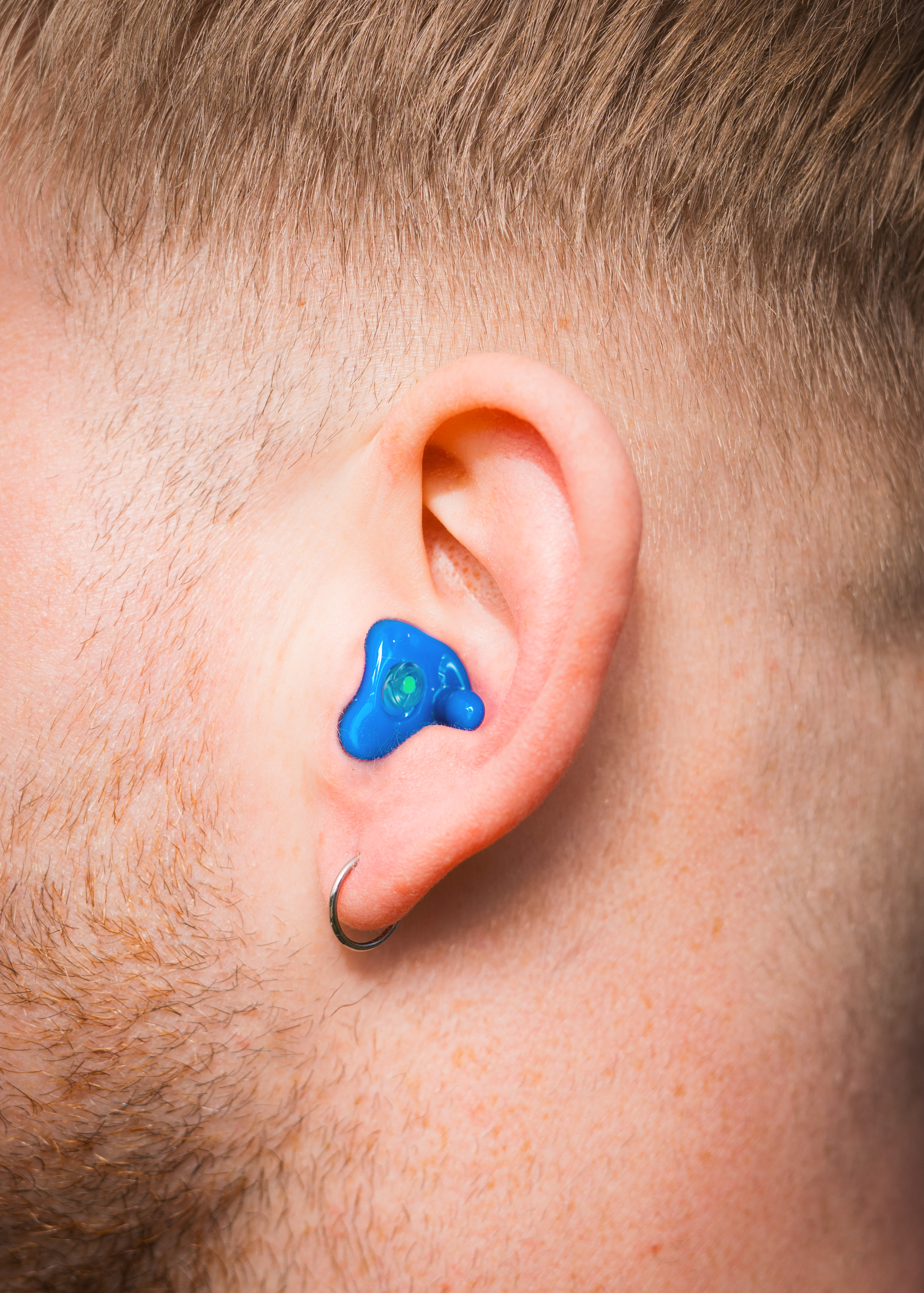 Alpine custom earplug worn in the ear, close-up of a man with short hair