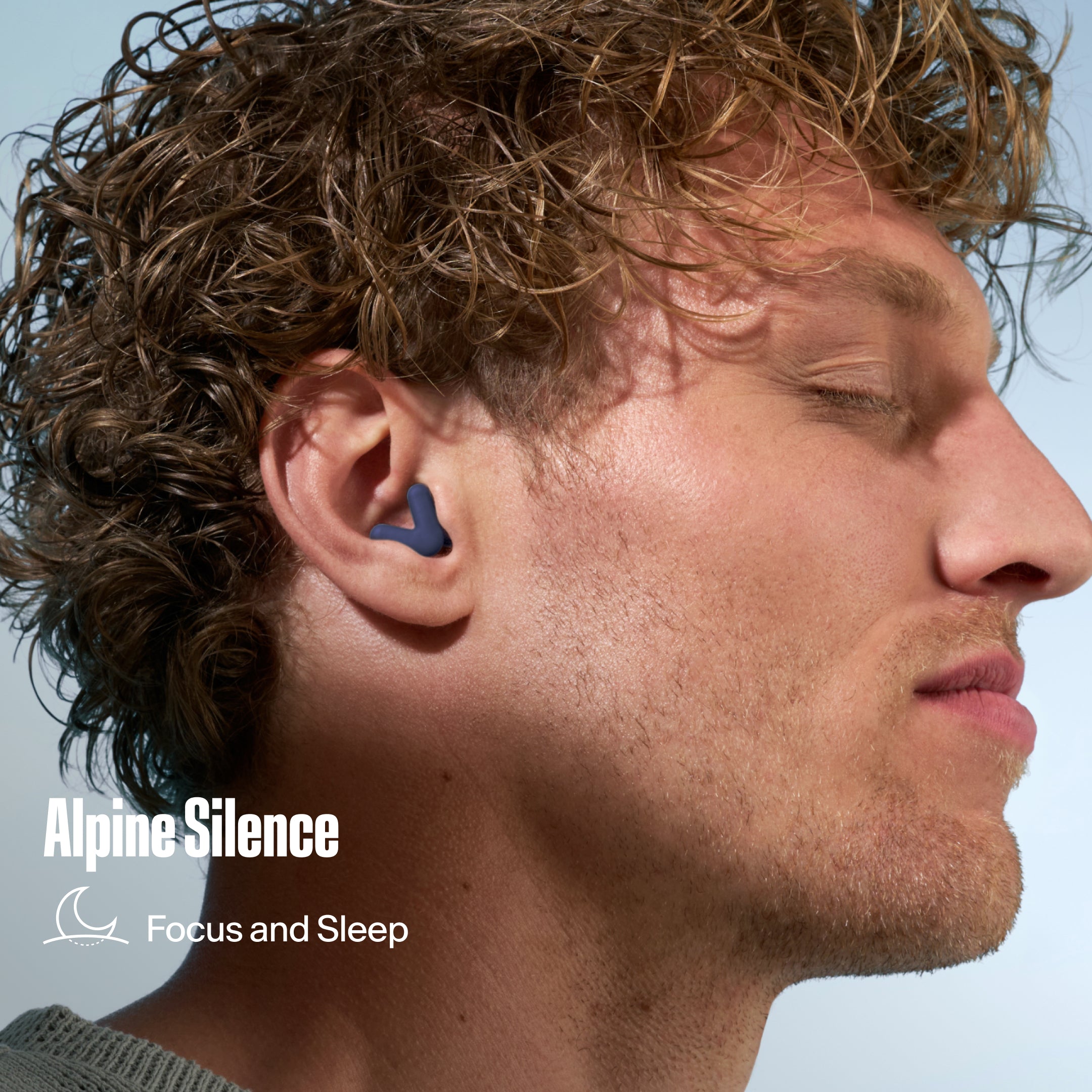 Alpine Silence earplug worn in the ear by a man with curly hair, with the text &