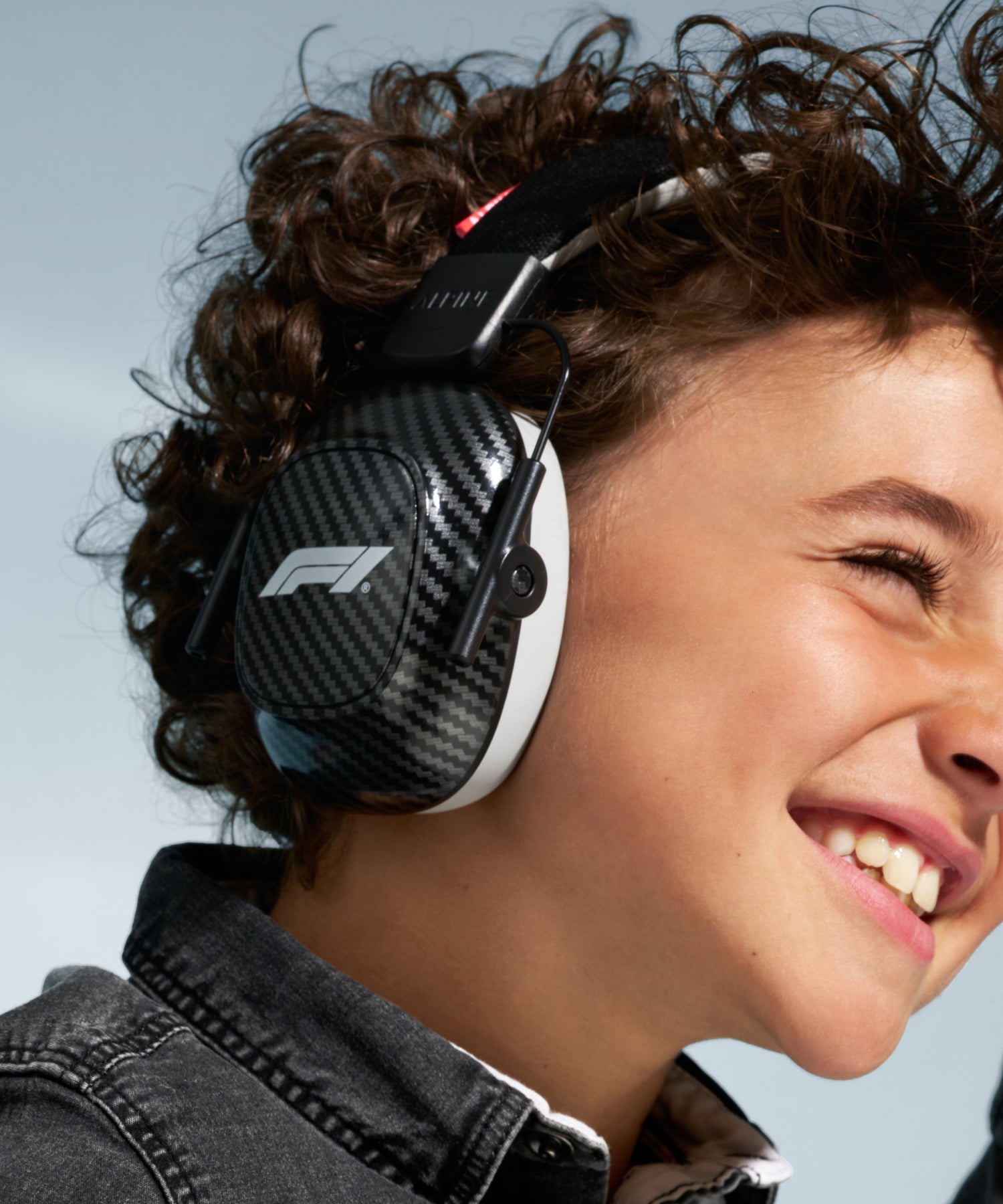 Smiling child with curly hair wearing Alpine Formula 1 Racing Muffy earmuffs with F1 logo 