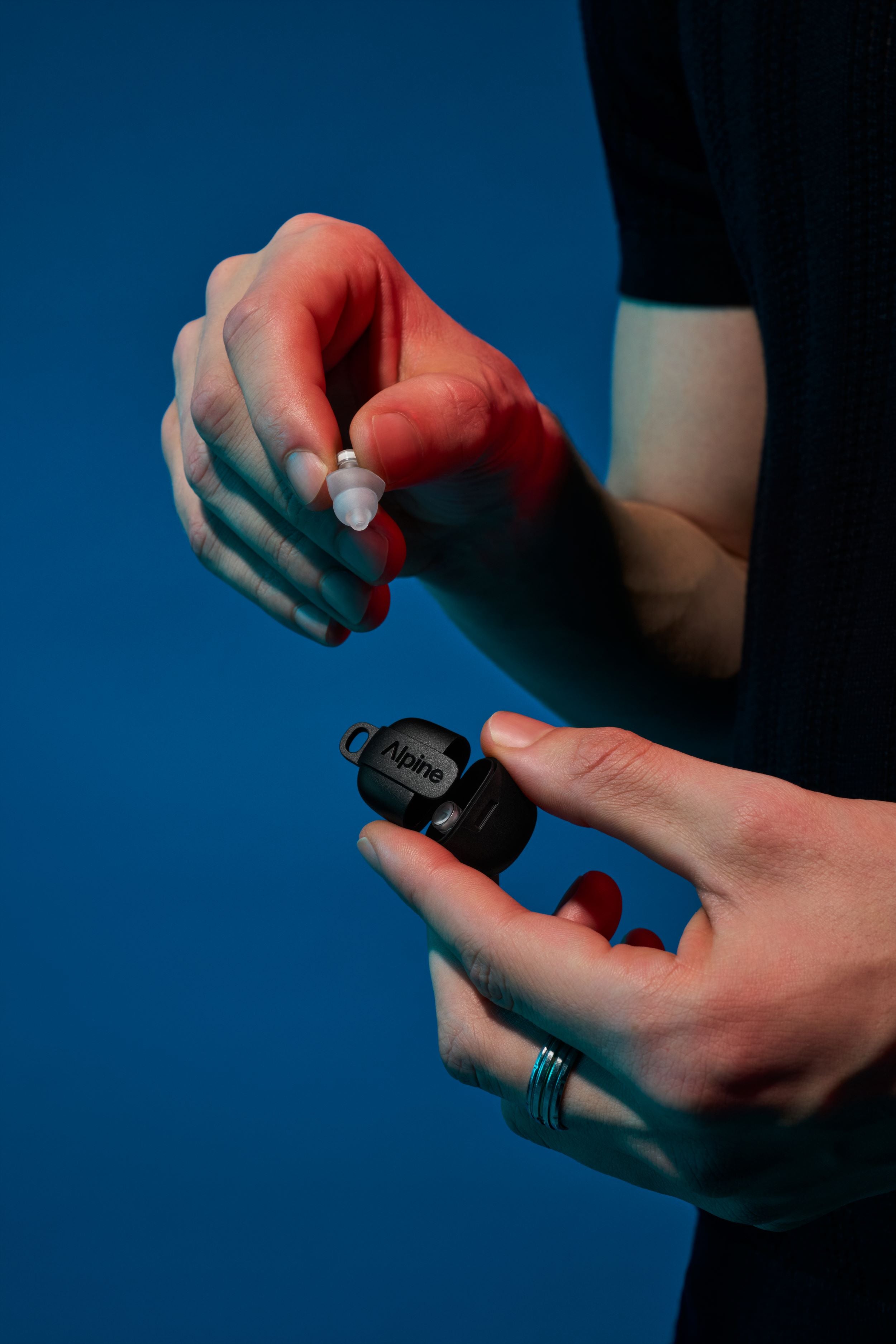 Alpine PartyPlug Pro Transparant earplug taken out of its case by a person against a blue background 